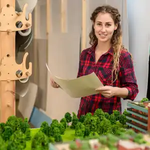 eine junge Architektin steht vor einem Planungsmodell mit Bäumen und Häusern