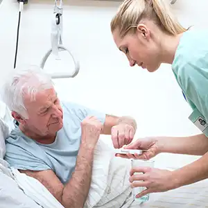 eine Pflegerin reicht einem Senioren im Bett seine Medikamente