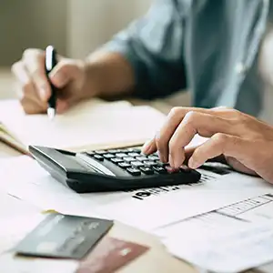 Person tippt auf Taschenrechner und hält Stift über Unterlagen.