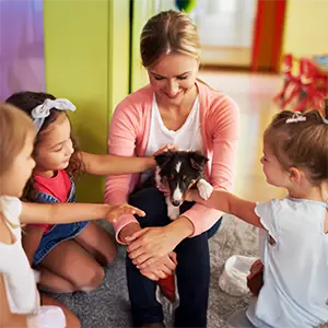 Welpe auf dem Schuß der Therapeutin wird von Kindern gestreichelt