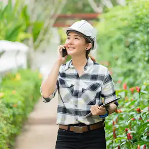 junge Frau mit Schutzhelm und Klemmbrett lächelt und telefoniert