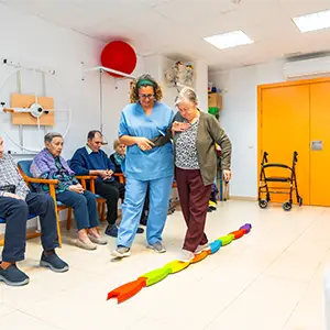 Ergotherapeut hilft älterer Dame beim Gehen auf einem bunten Übungsband.