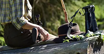 Jägerin sitzt neben dem Hut und Fernglas auf einem Baumstamm
