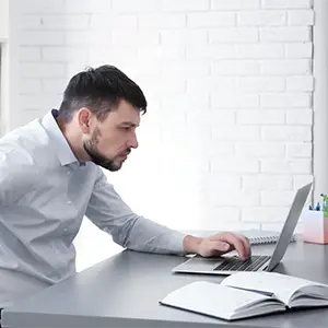 Rechtsschutzversicherung: Rechtliche Unterstützung bei Konflikten Ein Mann arbeitet am Laptop und hat Rückenschmerzen