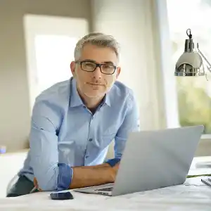 ein Mann sitzt vor seinem Laptop und blickt in die Kamera