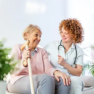 Pflegerin lachend neben ihrer Patientin auf der Couch