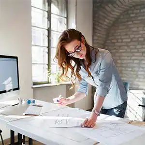 Frau steht im Büro über ihren Schreibtisch gebeugt und liest in Unterlagen