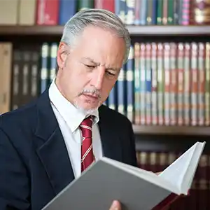 ein Anwalt steht in seiner Bibliothek und liest in einem Buch
