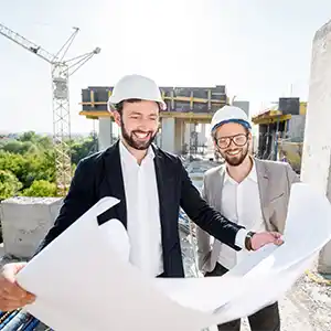 zwei Männer mit Bauhelm und Anzug betrachten einen Bauplan