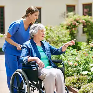 Pflegerin und Patientin im Rollstuhl gehen draußen spazieren